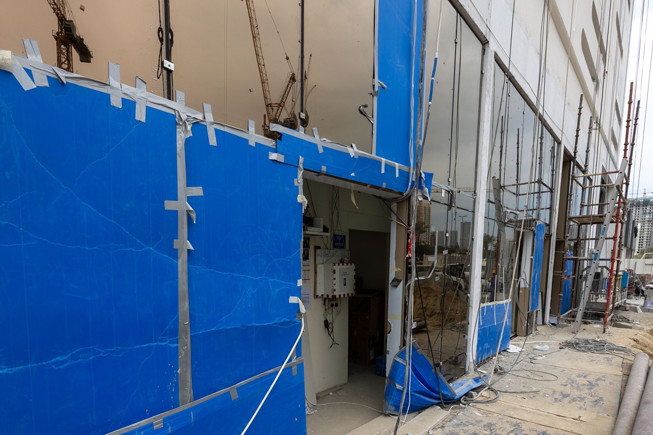 Pearl House By Imtiaz A construction site with blue tarpaulin covering broken windows, scaffolding, and visible electrical equipment inside.